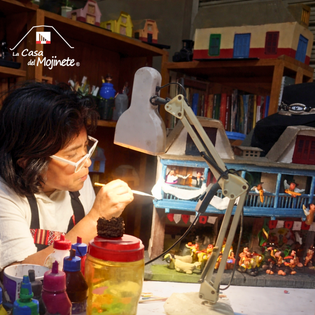 Artesana pintando a mano un retablo en miniatura con iluminación de lámpara en taller de artesanía.