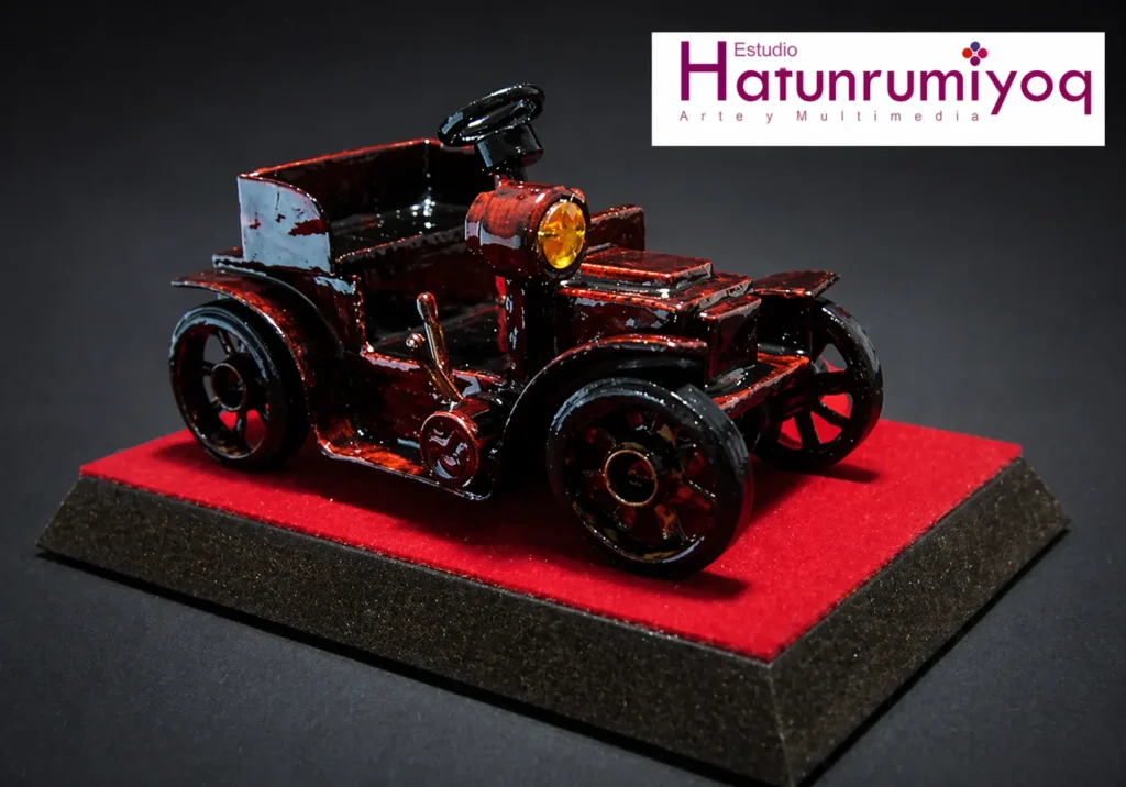 Maqueta artesanal de auto antiguo creada por Sergio Loaiza sobre base roja con fondo oscuro en estudio